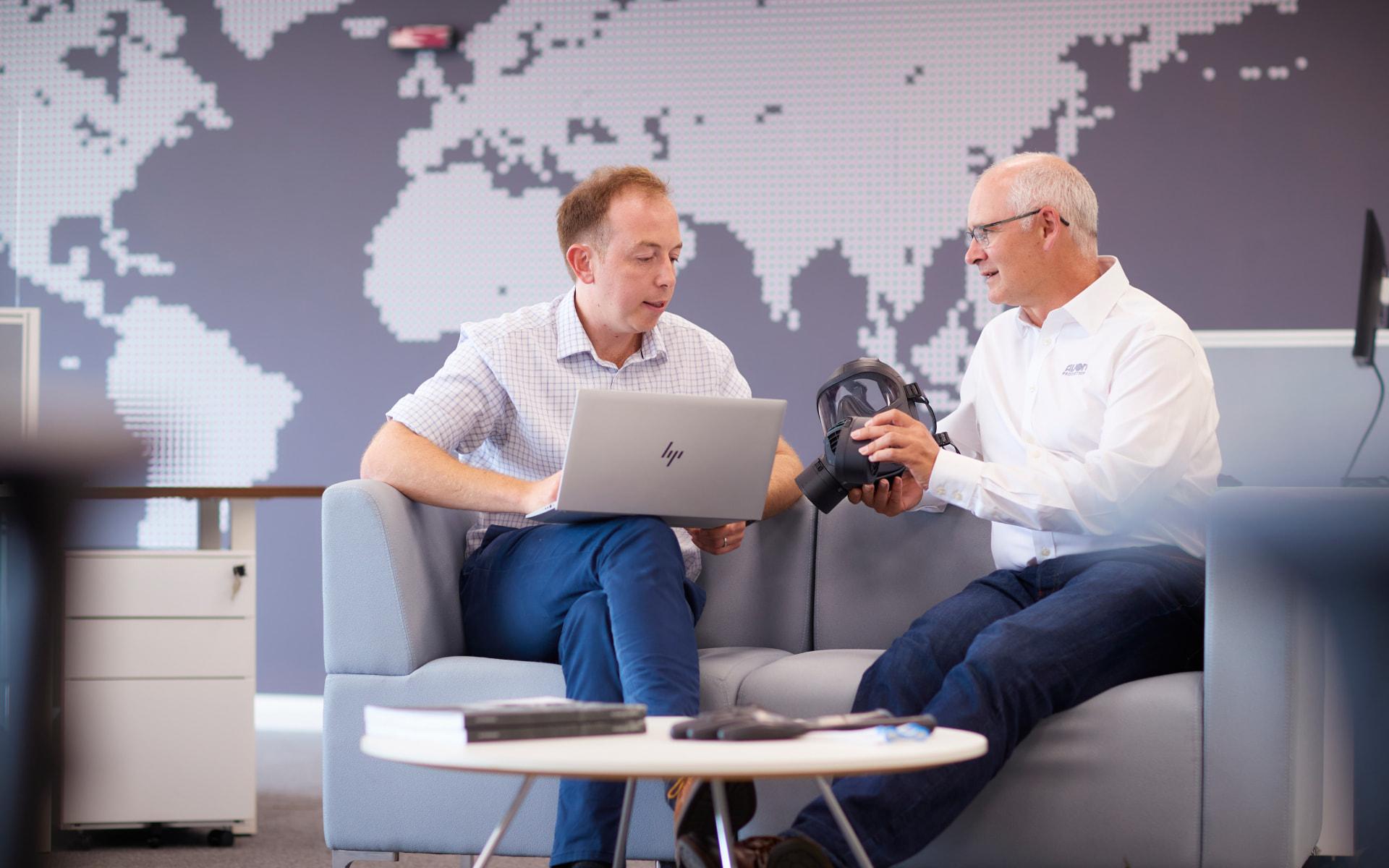 Two employees sat in an office looking at a respirator and laptop